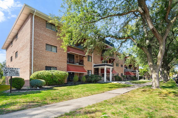 Front view of a multi-story brick apartment building with red awnings and a covered entrance.