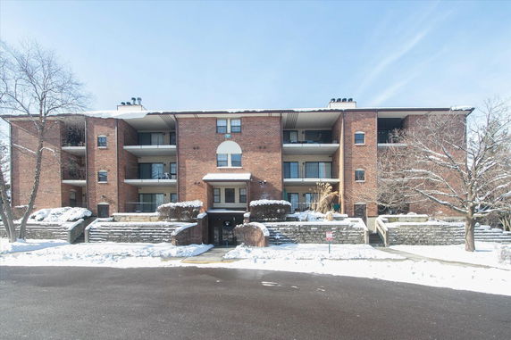 Front view of a multi-story brick apartment building with balconies and a central entrance, surrounded by snow-covered ground.