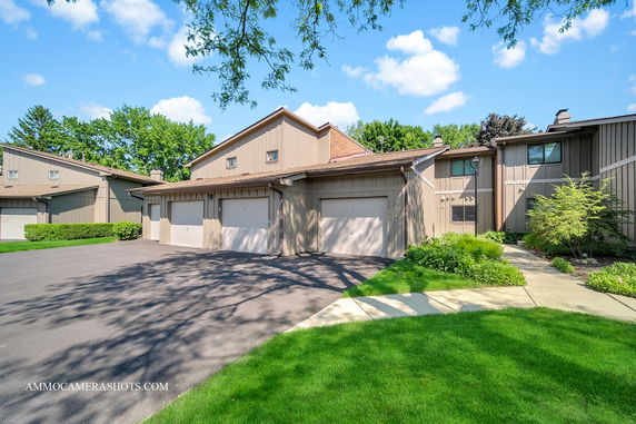 Front view of a multi-unit building with garages and a well-maintained lawn.