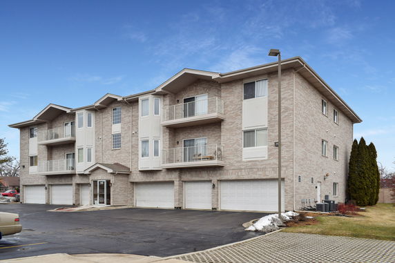Front view of a three-story apartment building with balconies and garages on the ground level.