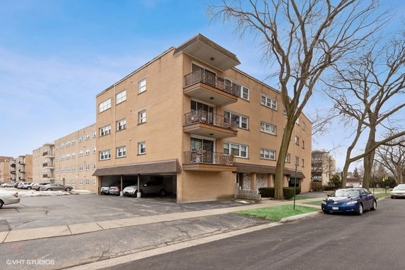 Front view of a multi-story apartment building with balconies and parking area underneath.