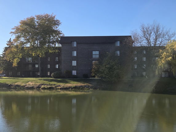 Front view of a multi-story apartment building near a pond.