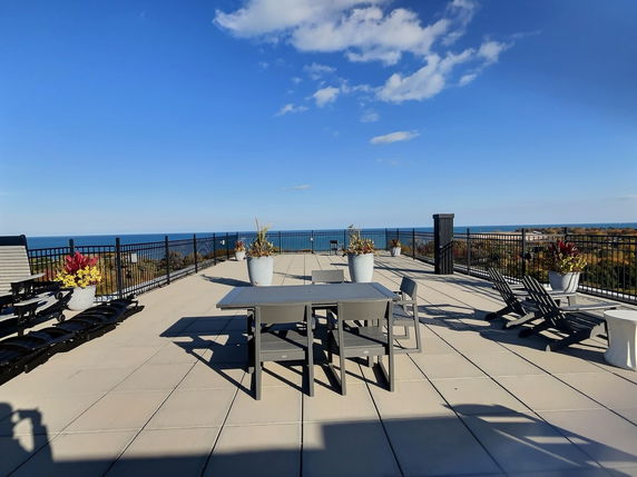 Rooftop area with tables, chairs, and lounge chairs, offering a view of the ocean.