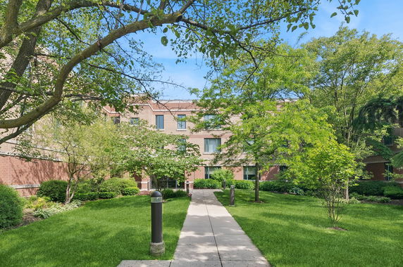 Front view of a multi-story brick building with a walkway and landscaped surroundings.