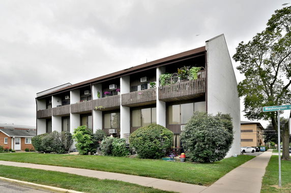 Front view of a three-story apartment building with balconies and plants.