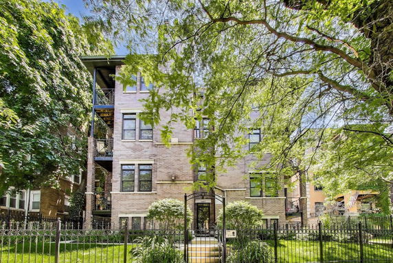Front view of a multi-story brick building with large windows and a gated entrance.