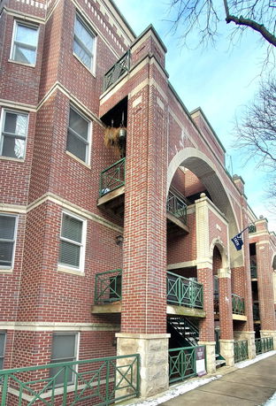 Front view of a multi-story brick building with green railings and arched design elements.