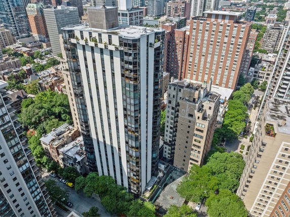 Aerial view of a tall, modern building with adjacent city structures and greenery.