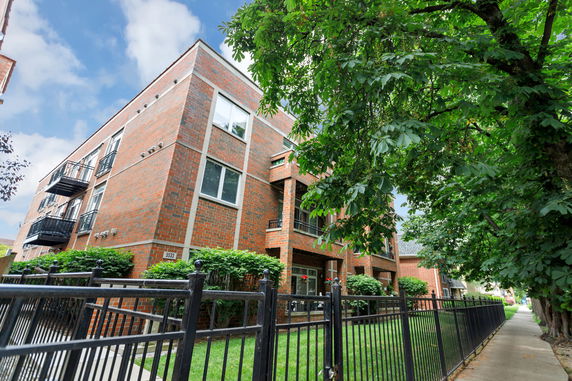 Front view of a brick apartment building with balconies and a fenced yard.
