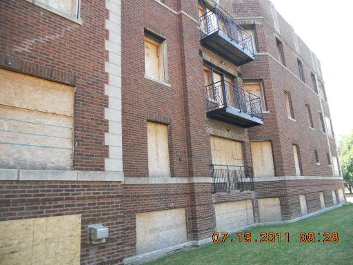 Side view of a multi-story brick building with boarded-up windows and balconies.