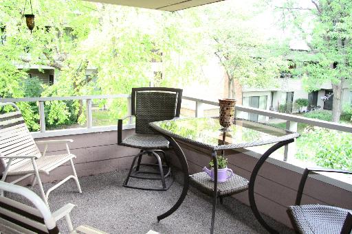 Outdoor patio area with chairs and a table overlooking trees and adjacent buildings.