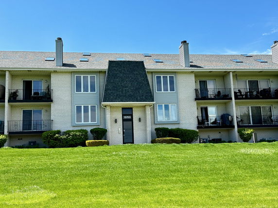 Front view of a multi-story apartment building with balconies and a pitched roof.