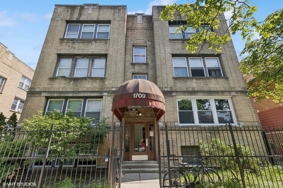 Front view of a three-story brick apartment building with an arched entrance.
