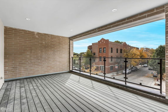 Panoramic view from a modern balcony overlooking a street with brick buildings.