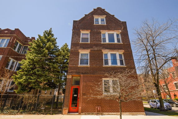Front view of a three-story brick apartment building with a red door entry.