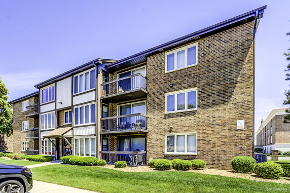 Front view of a three-story brick apartment building with balconies.