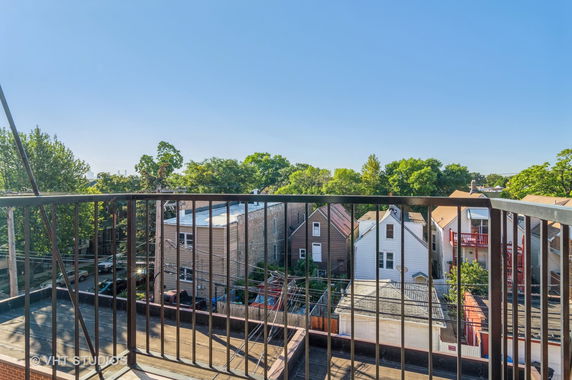 View from a balcony overlooking residential rooftops and trees.