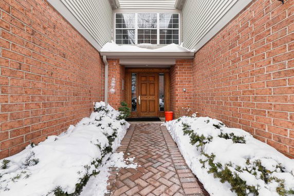 Front entrance of a brick house with a brown door under snowy conditions.
