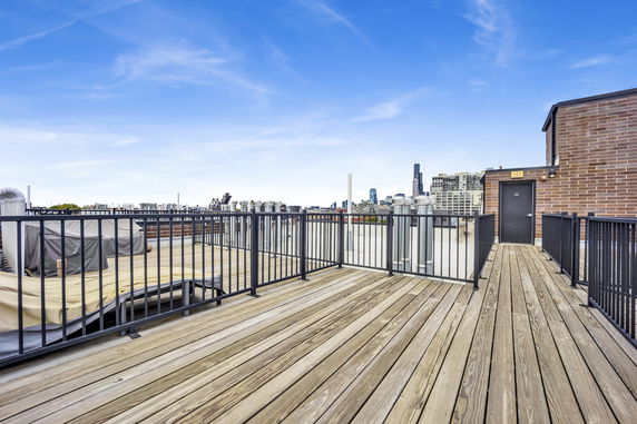 Wooden deck rooftop with metal railing and city skyline in the background.