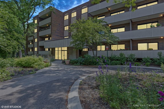 Front view of a multi-story building with balconies and large windows, surrounded by trees and plants.