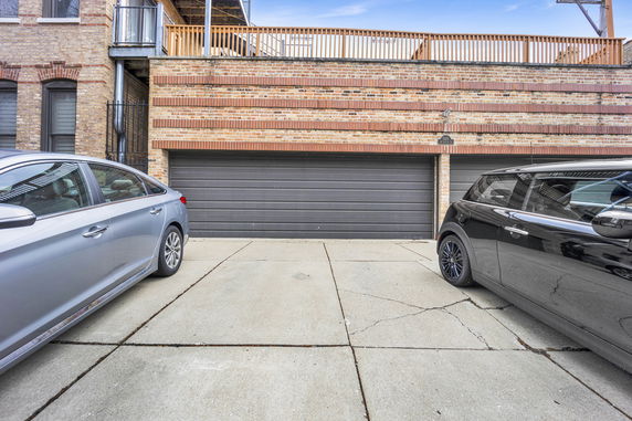 Two parked cars in front of a double garage in a brick building.