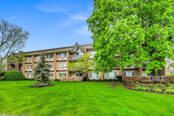 Front view of a multi-story apartment building with brick exterior and a sign displaying the number 320.