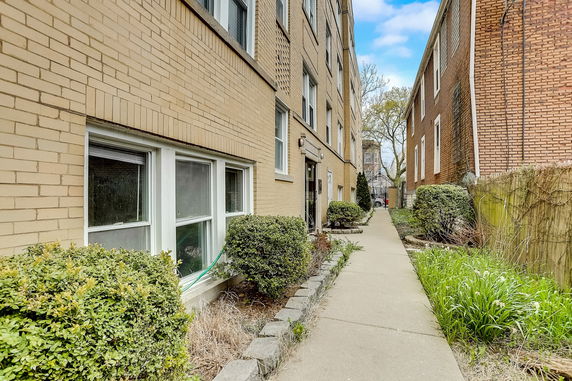 Front view of a brick residential building entrance along a walkway.