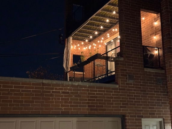 Night view of a building with a brick facade and a balcony decorated with string lights.