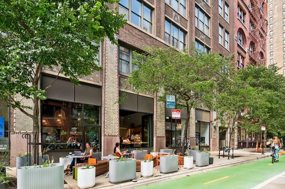 Front view of a multi-story brick building with large windows and a street-level cafe.