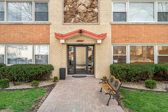 Front view of a brick building entrance with a walkway and a bench.