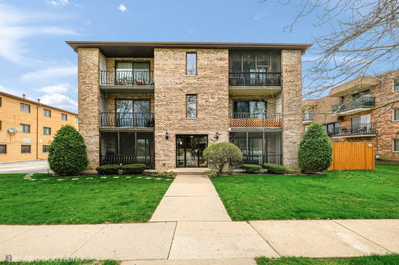 Front view of a three-story brick apartment building with balconies.