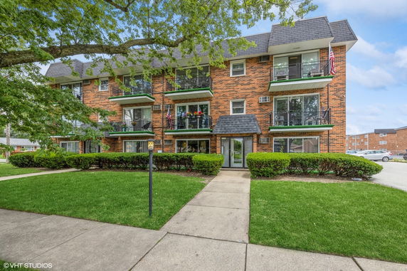 Front view of a multi-story brick apartment building with balconies and a central entrance.