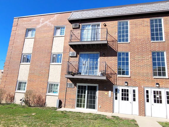 Front view of a three-story brick apartment building with balconies and multiple entrances.