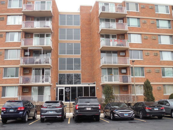 Front view of a multi-story apartment building with balconies and parked cars.