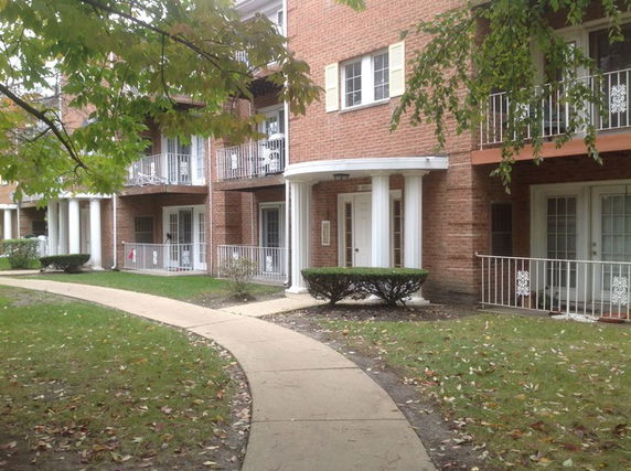 Front view of a multi-story brick residential building with balconies and a walkway.