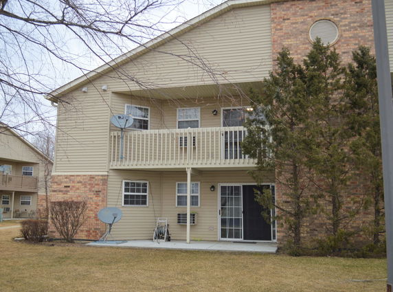 Two-story house with beige siding and brick accents, featuring a balcony and a sliding glass door on the ground level.