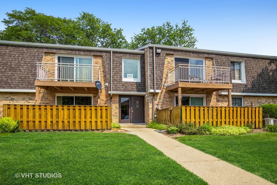 Front view of a two-story residential building with balconies and a fenced area.
