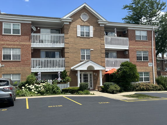 Front view of a three-story brick apartment building with balconies and a parking area.
