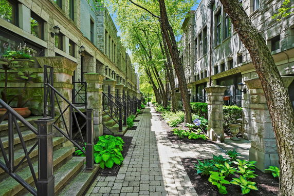 Front view of a row of townhouses with stone facades and railings along an outdoor pathway.