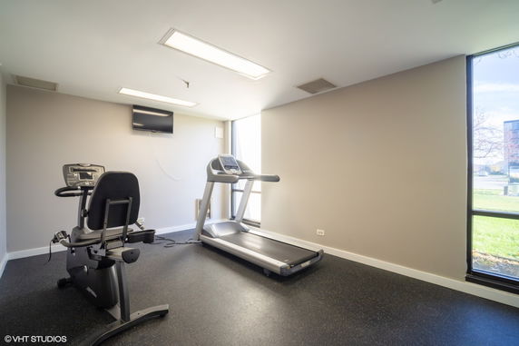 Room with gym equipment including a treadmill and exercise bike.