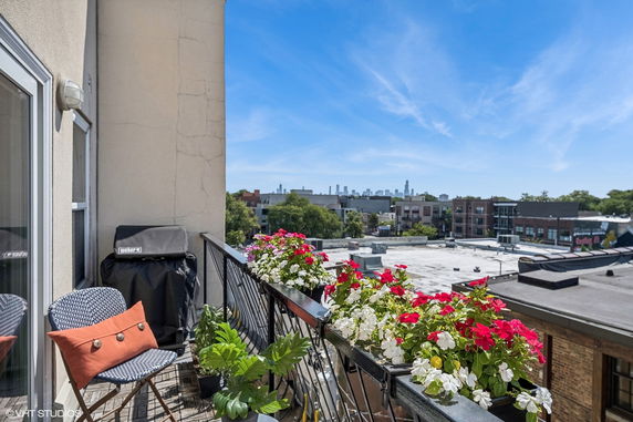 View from a balcony with flowers and patio furniture overlooking buildings and city skyline.