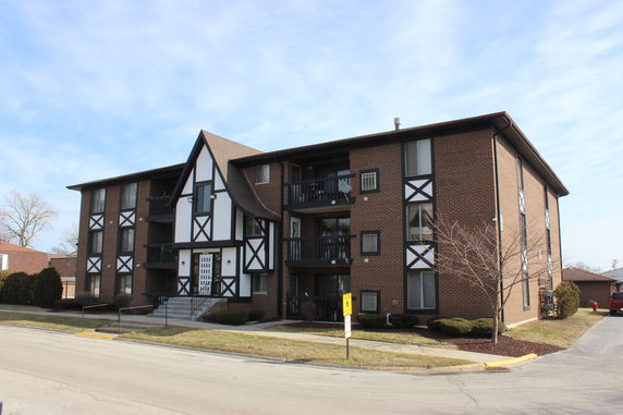 Front view of a three-story apartment building with a brick exterior and decorative white and black trim.