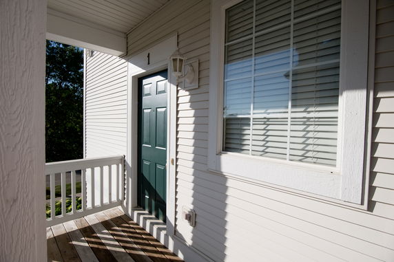 Front view of a building entrance with a green door and window with blinds.