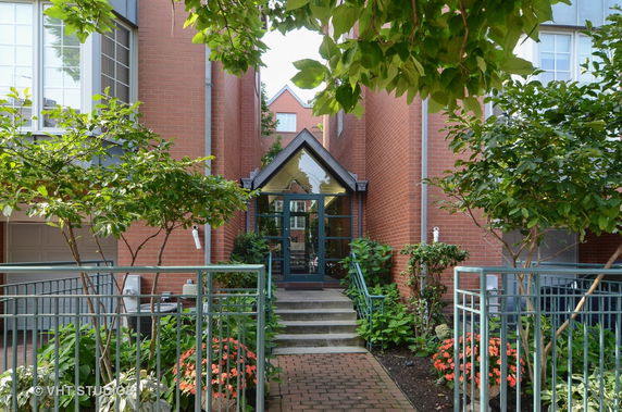 Front view of a brick building entrance with a glass door and steps leading up.