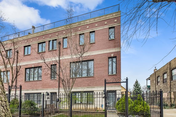 Front view of a multi-story brick building with large windows and a gated entrance.