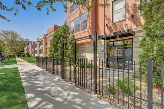 Front view of a multi-story building labeled 'Claremont Lofts' with a glass entrance and metal fencing.