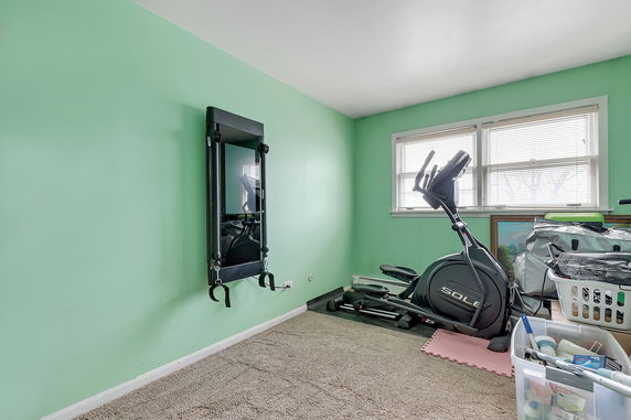 Room with exercise equipment including a stationary bike and wall-mounted fitness mirror.