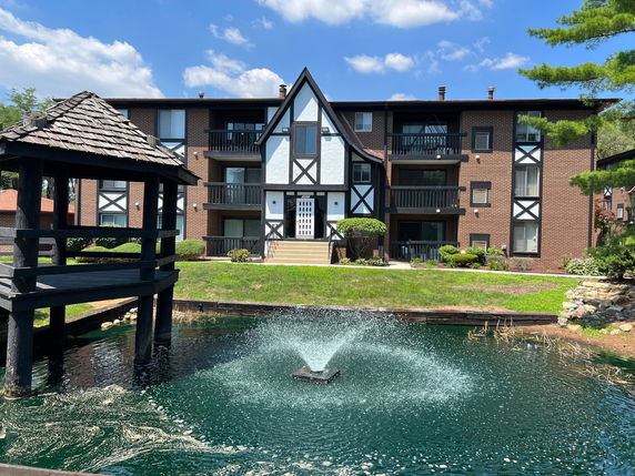 Front view of a multi-story building with a brown and white exterior and a pond with a fountain in front.