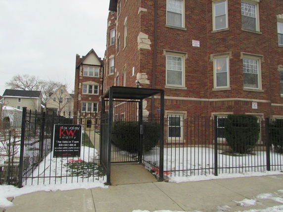 Front view of a multi-story brick apartment building with gated entrance.
