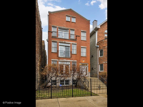 Front view of a multi-story brick house with iron railings and a small front yard.